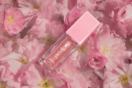 Petal Pop Bloom Lip Oil resting on soft pink flowers